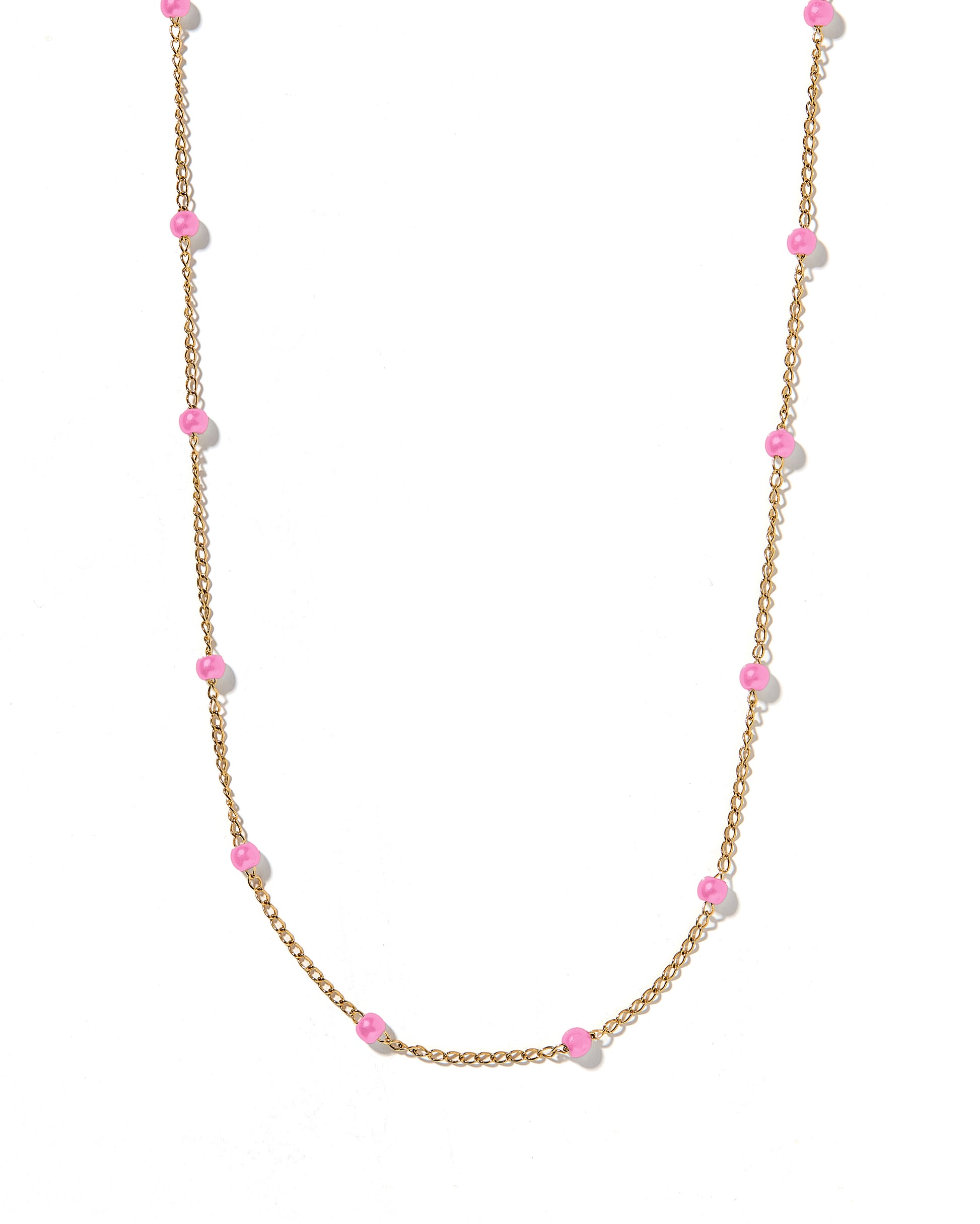 A gold chain necklace with pink bead accents laid out on a white surface.