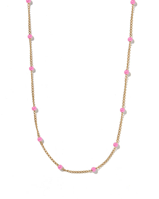 A gold chain necklace with pink bead accents laid out on a white surface.