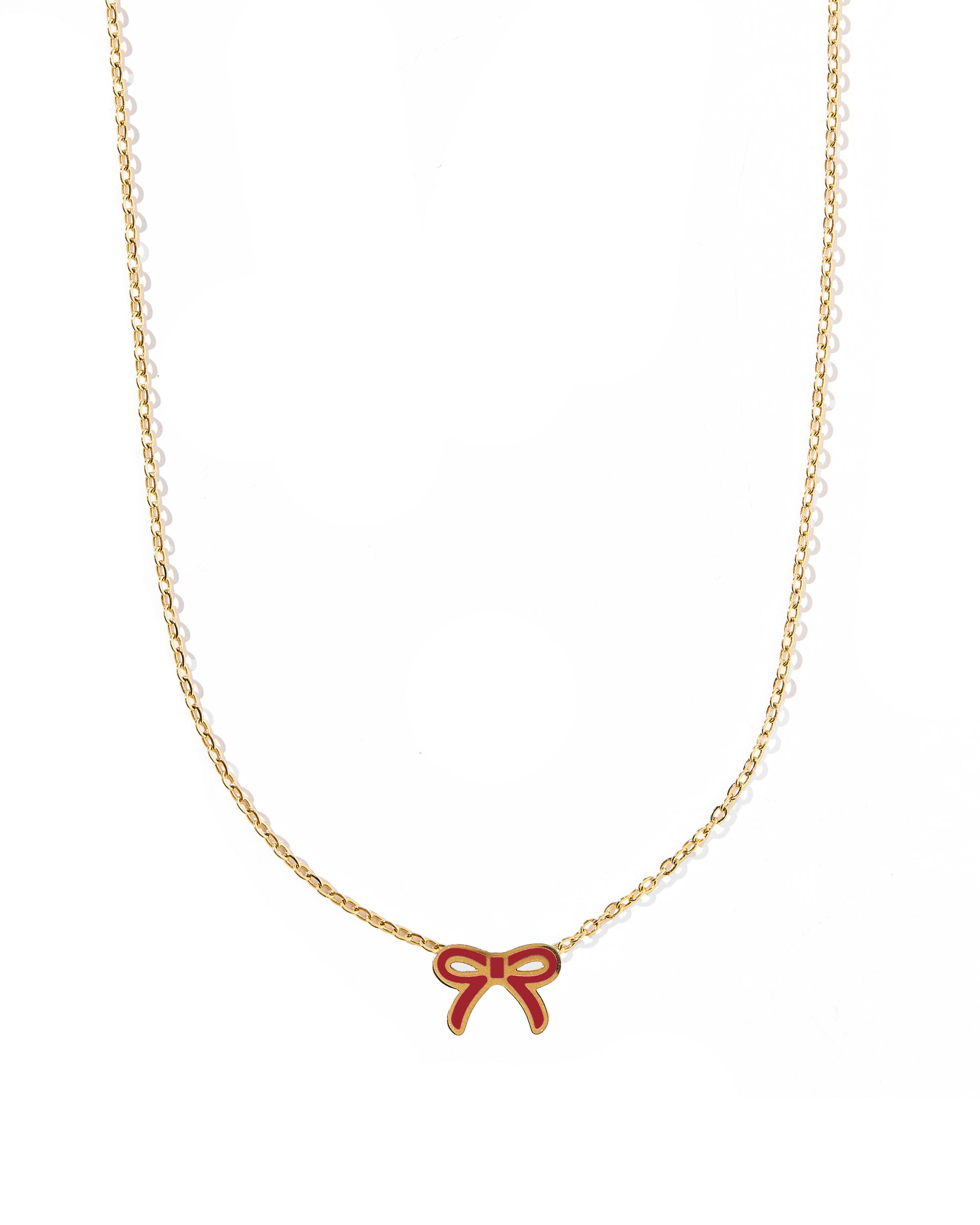 A thin gold bow pendant necklace with a maroon bow at the end, displayed against a white background.