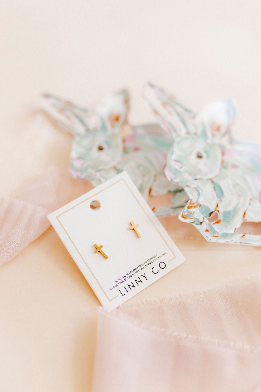 LINNY CO Catherine Cross Gold screwback stud earrings — hypoallergenic, waterproof stainless steel, flat-lay styling.