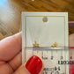 Gold dragonfly-shaped earrings on a card with a ruler for scale, held by a person with red nail polish.