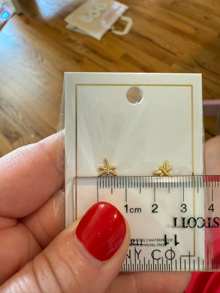 Gold dragonfly-shaped earrings on a card with a ruler for scale, held by a person with red nail polish.