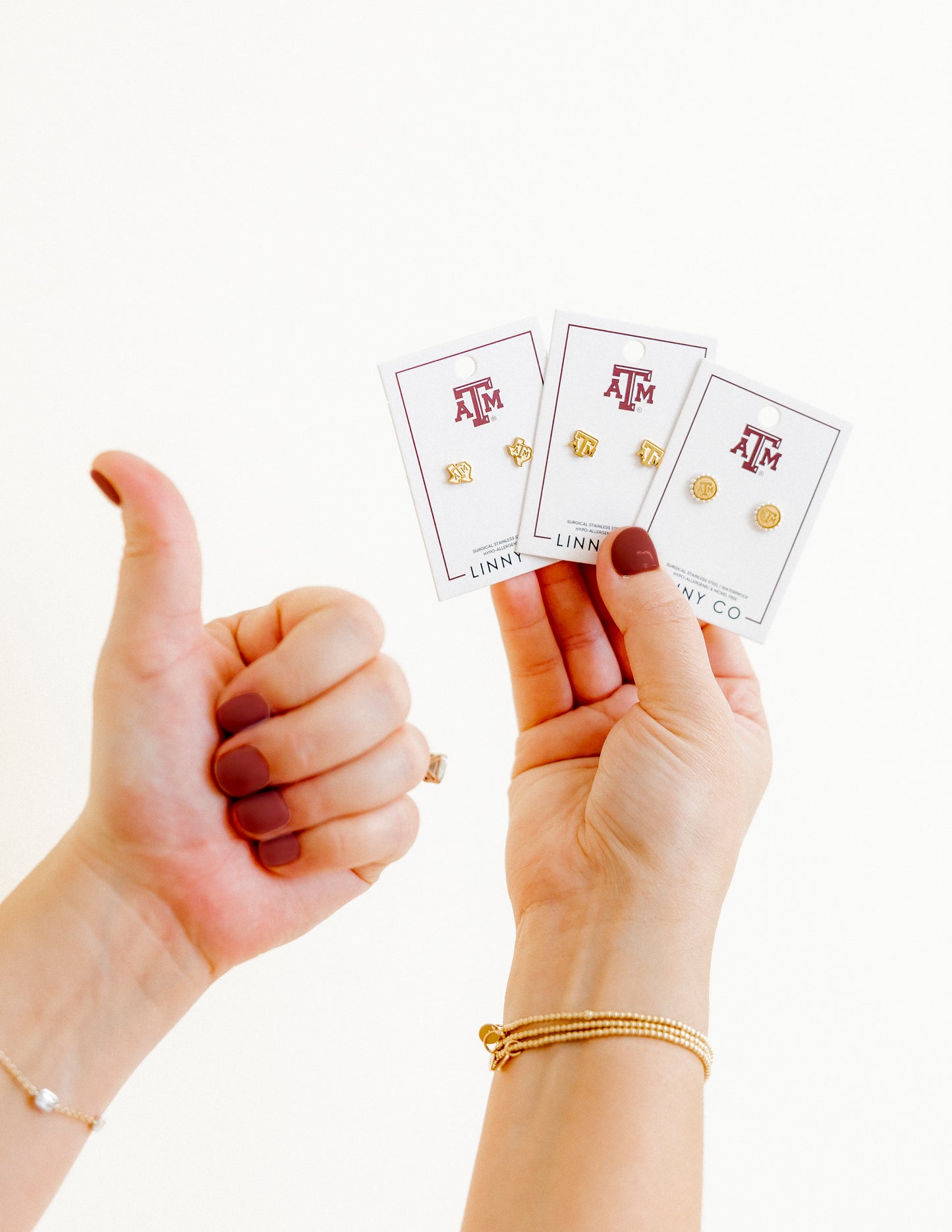 Two hands holding three cards with earrings on a white background