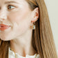 Close-up of a woman wearing gold earrings and a necklace against a neutral background