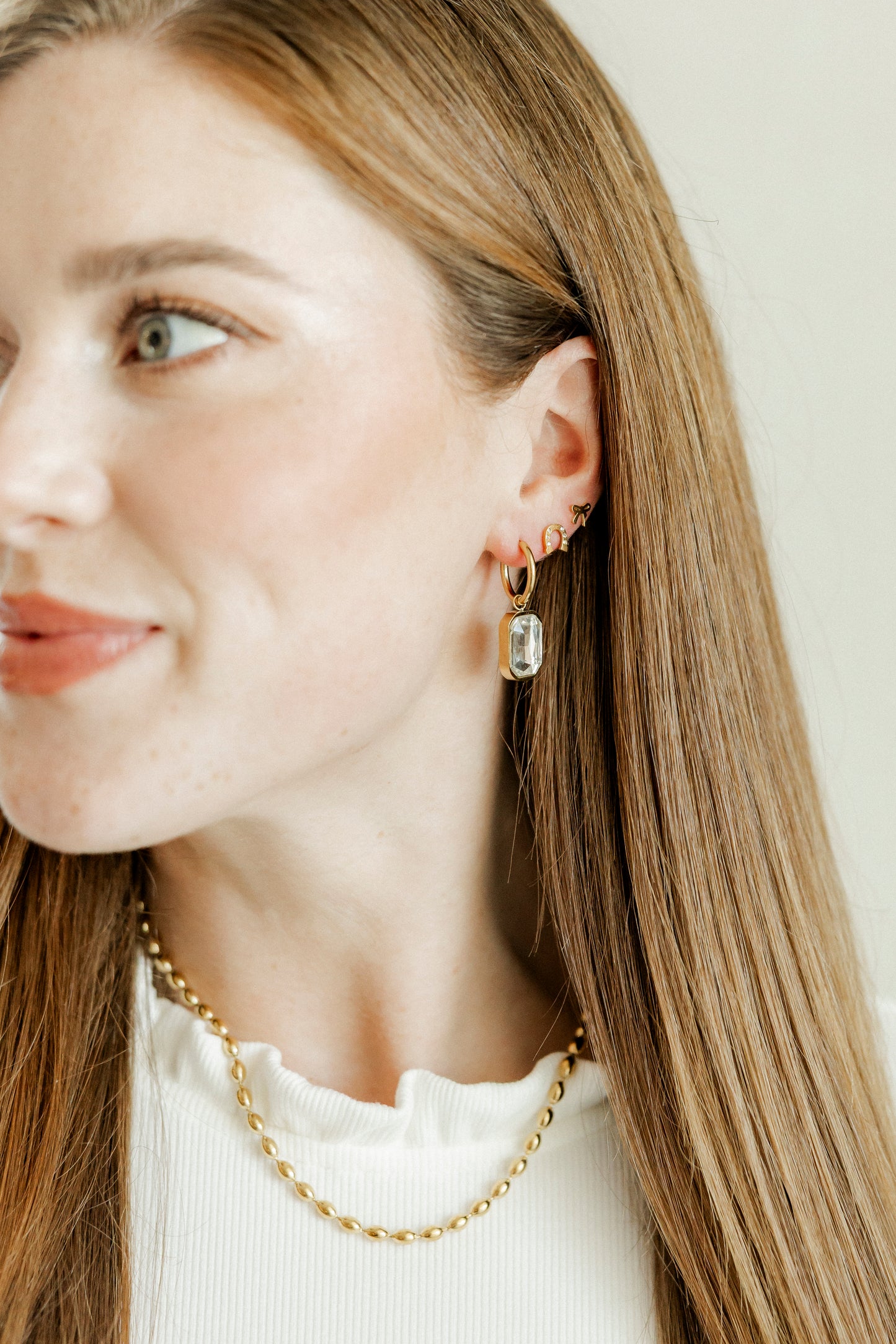 Close-up of a woman wearing gold earrings and a necklace against a neutral background