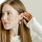 Woman wearing gold earrings and a ring, with a neutral background