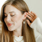 Woman wearing gold earrings and a necklace, with a neutral background
