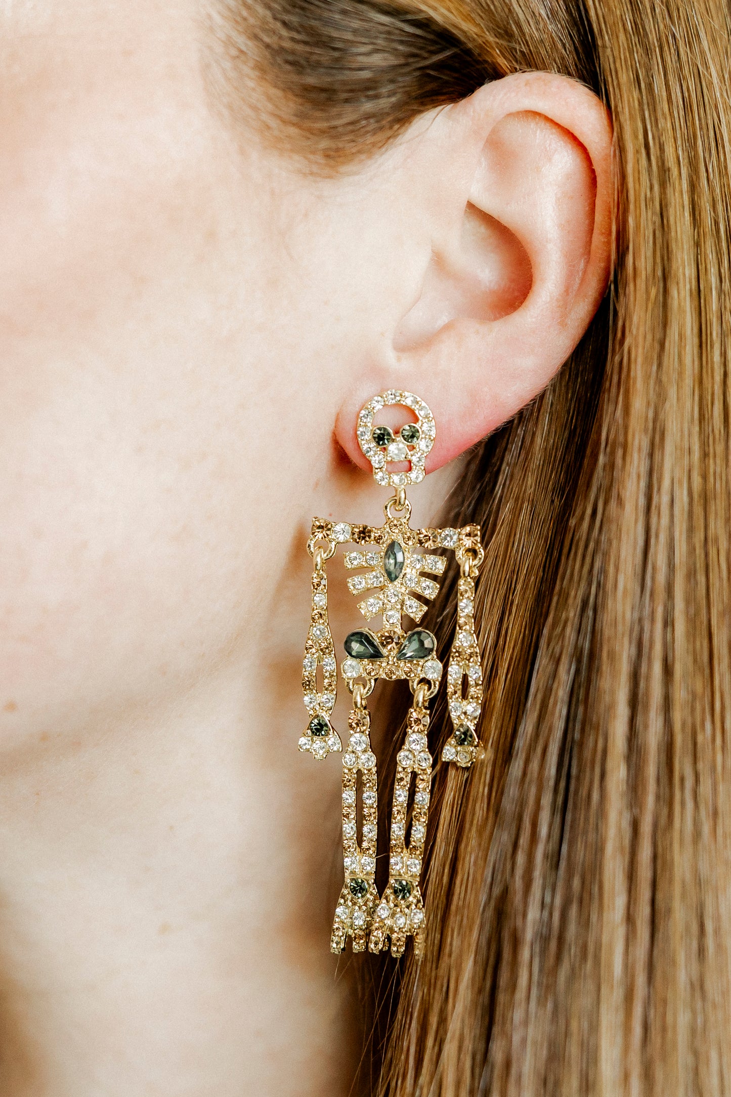 Close-up of a person wearing an ornate earring with green gemstones.