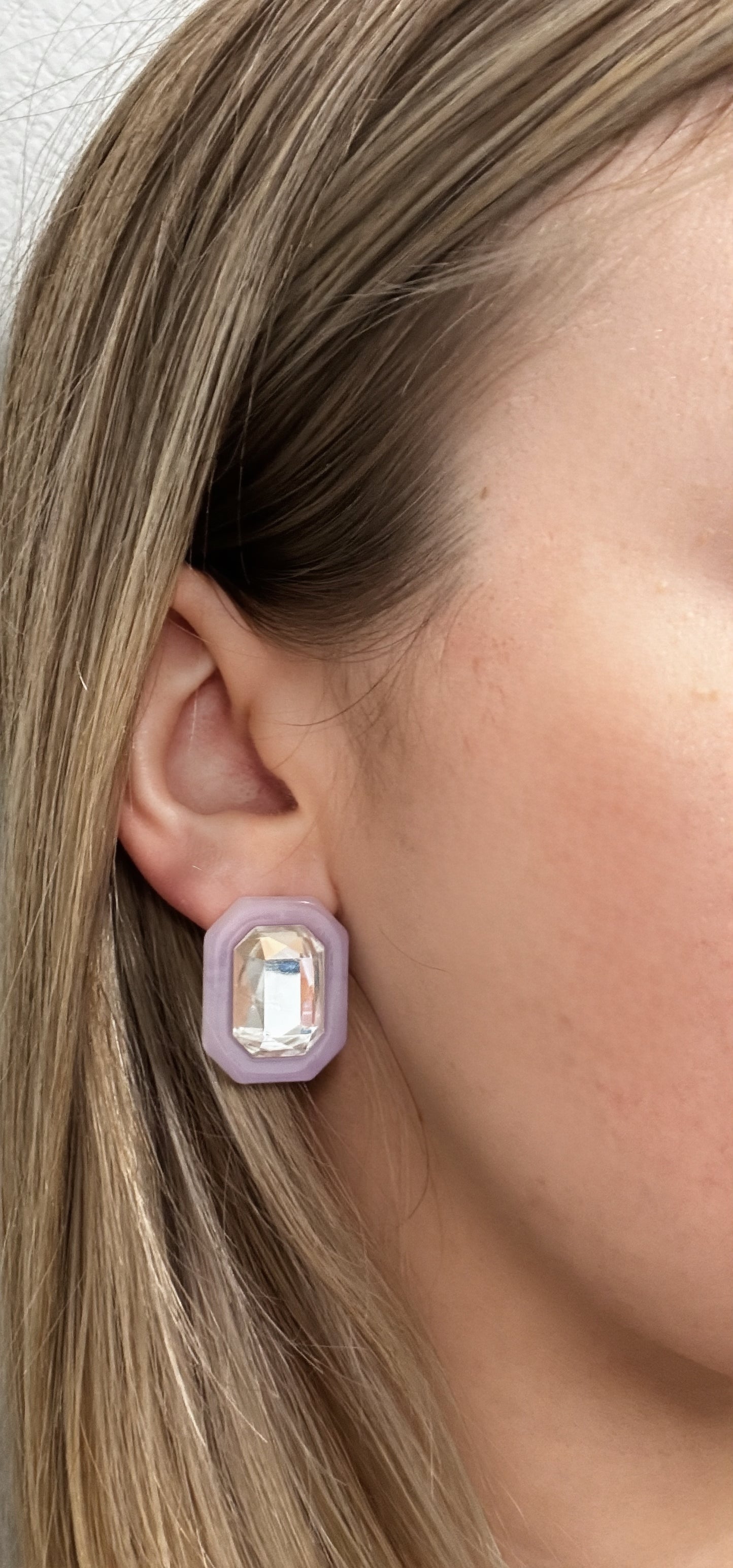 Close-up of an ear wearing a stud earring with a light purple frame and clear gemstone.