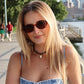 Woman wearing sunglasses and a denim dress by a waterfront with city skyline in the background