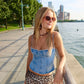 Woman in denim top and leopard print skirt standing by a waterfront with city skyline in the background