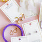 LINNY CO Nola 8mm huggie earrings for kids & little girls — hypoallergenic, waterproof stainless steel, flat-lay styling.