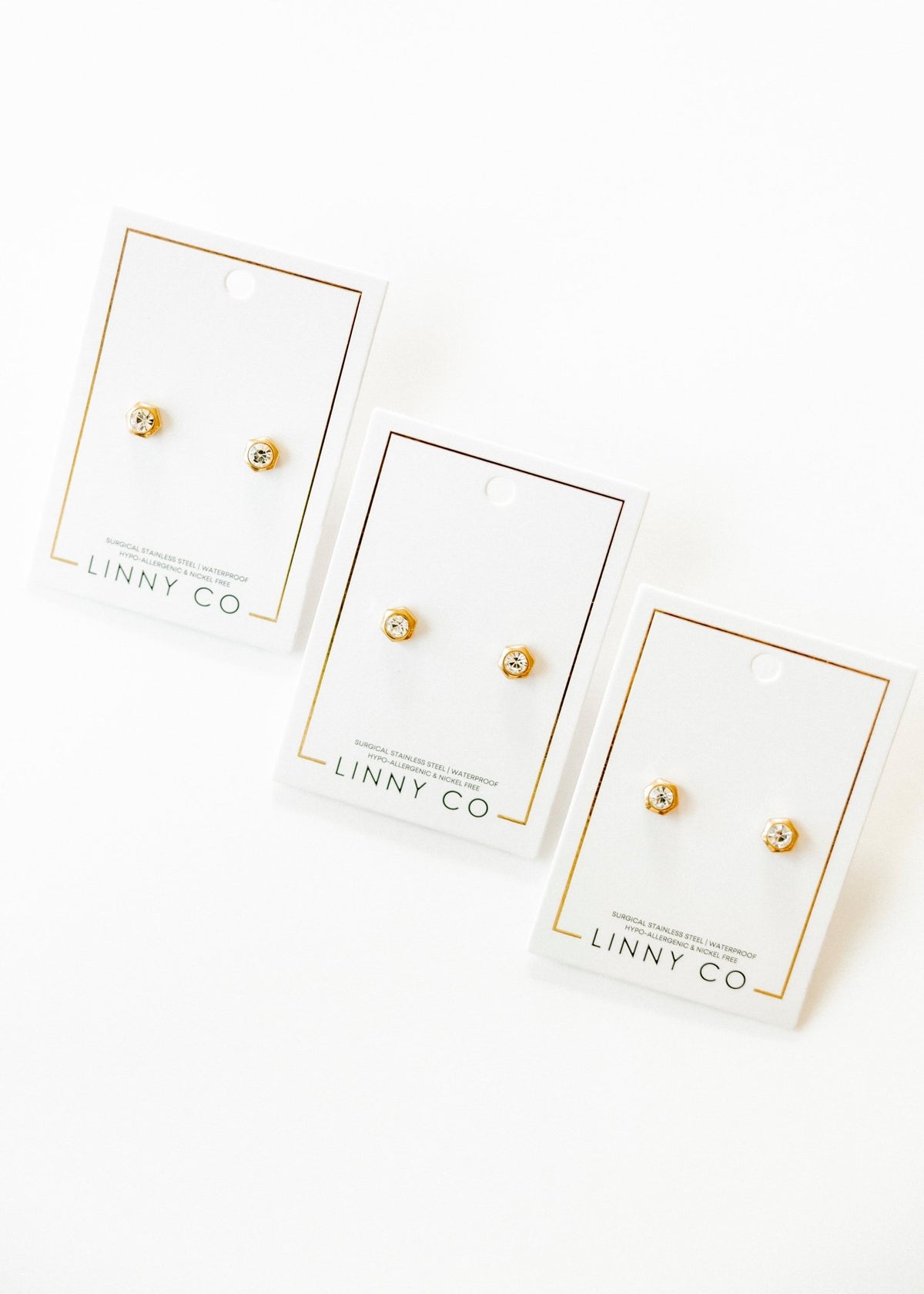LINNY CO Addison Clear Gold screwback stud earrings for kids & little girls — hypoallergenic, waterproof stainless steel with secure screwback backs, flat-lay styling.