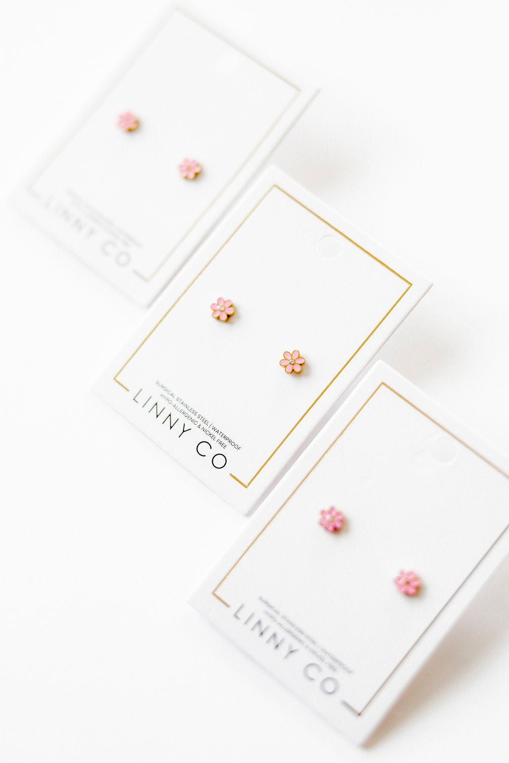 LINNY CO Alli Pink screwback stud earrings for kids & little girls — hypoallergenic, waterproof stainless steel with secure screwback backs, flat-lay styling.