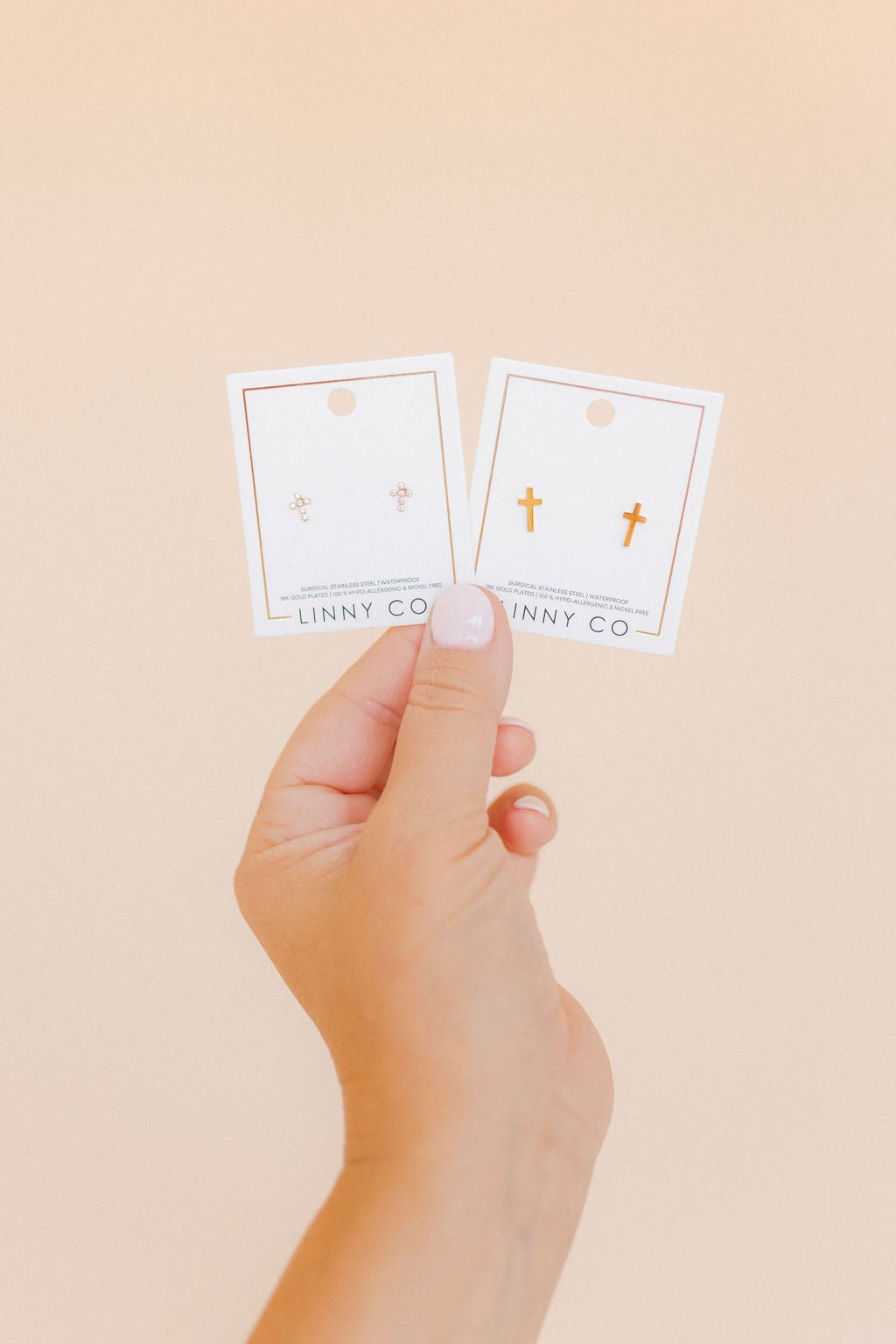 LINNY CO Catherine Cross Gold screwback stud earrings — hypoallergenic, waterproof stainless steel, in packaging.