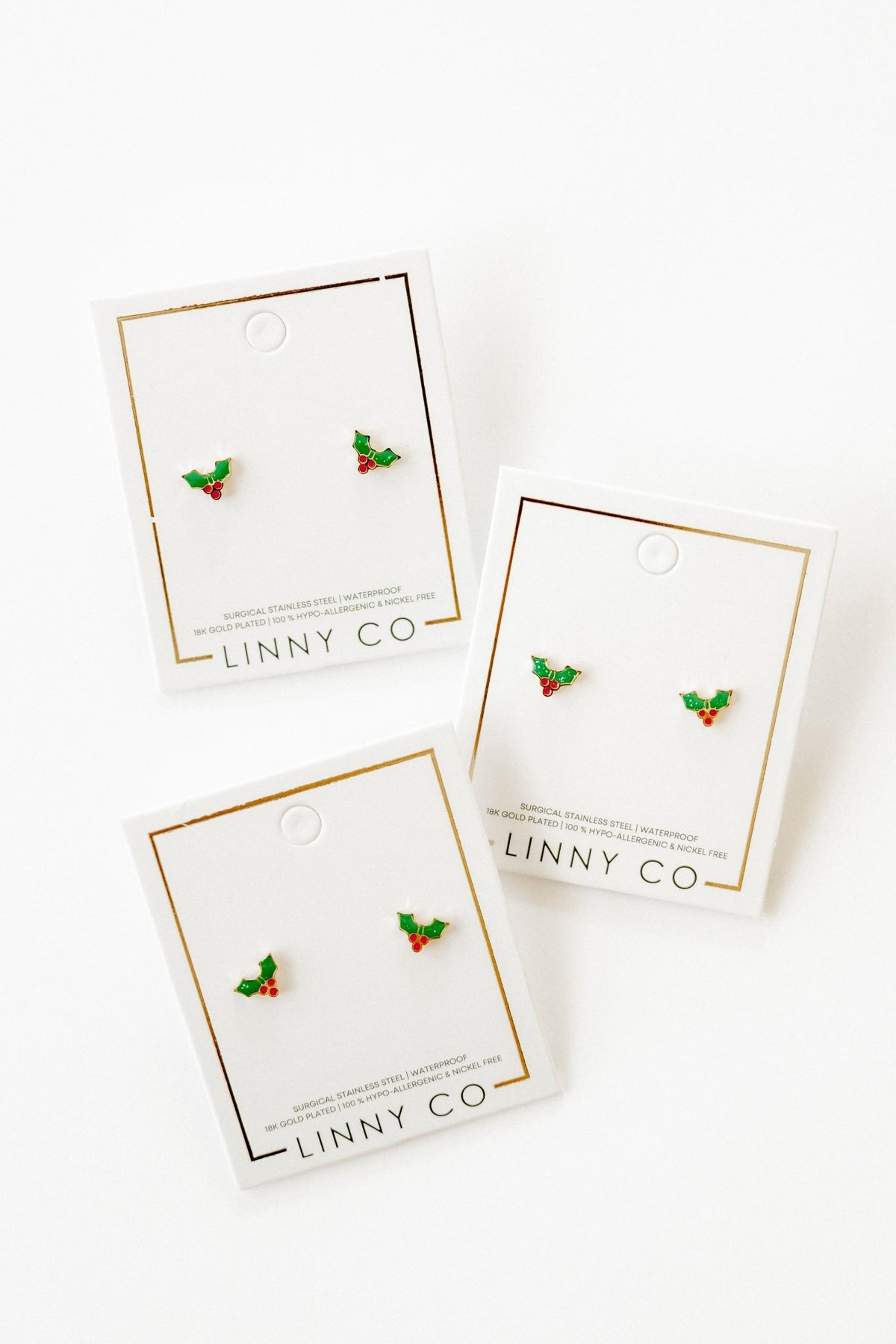 LINNY CO Holly Berry screwback stud earrings for kids & little girls — hypoallergenic, waterproof stainless steel with secure screwback backs, flat-lay styling.