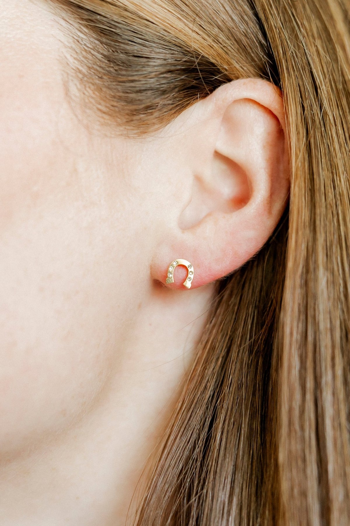 LINNY CO Horseshoe Gold screwback stud earrings for kids & little girls — hypoallergenic, waterproof stainless steel with secure screwback backs, shown on model.