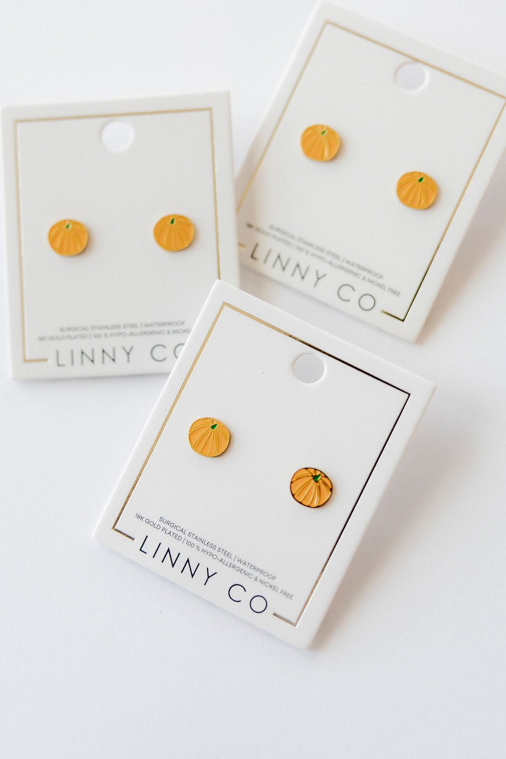 LINNY CO Knox Pumpkin screwback stud earrings for kids & little girls — hypoallergenic, waterproof stainless steel with secure screwback backs, flat-lay styling.