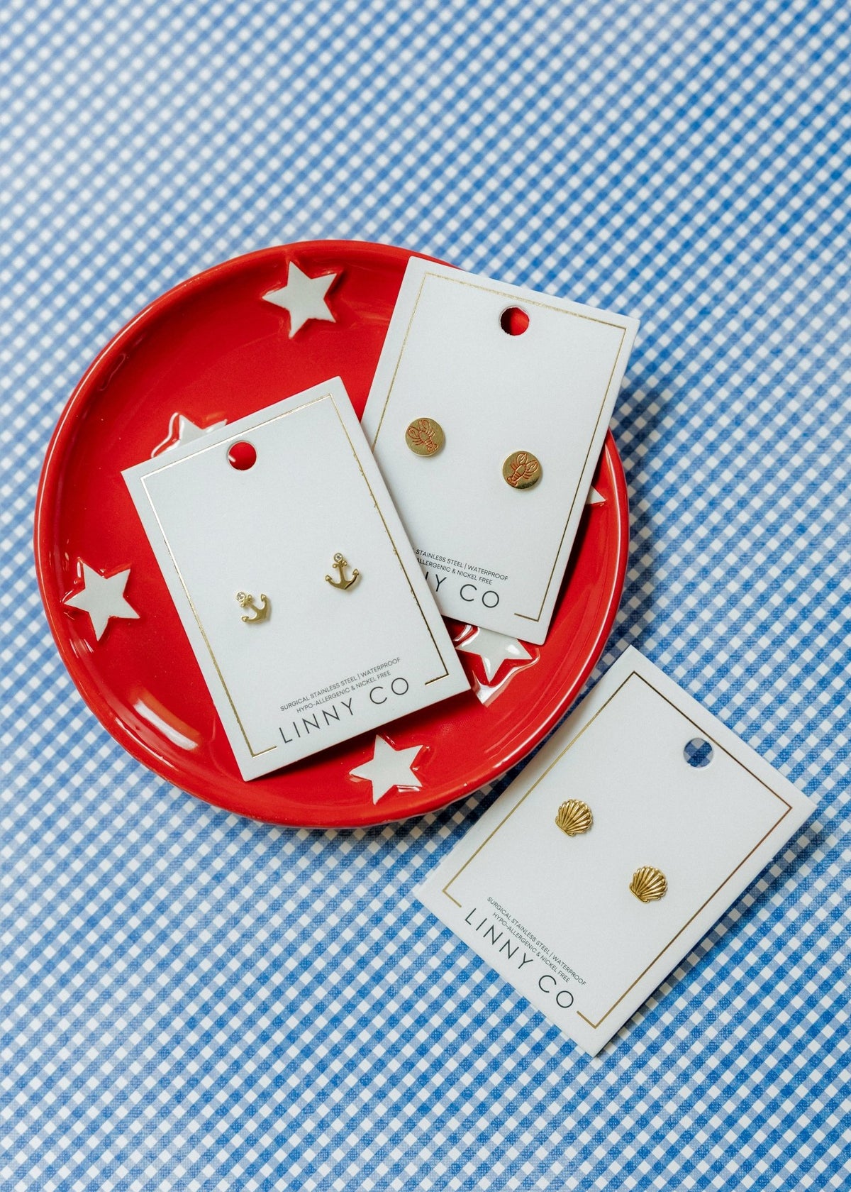 LINNY CO Marina Shell screwback stud earrings for kids & little girls — hypoallergenic, waterproof stainless steel with secure screwback backs, flat-lay styling.