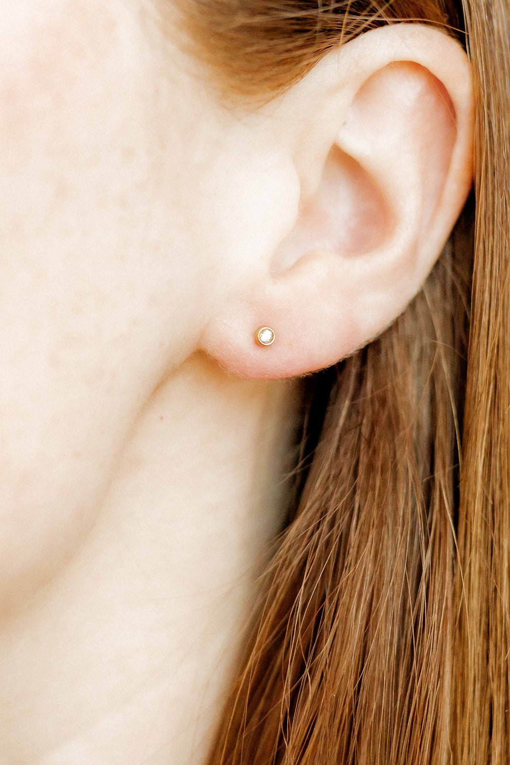 LINNY CO Micro Cooper Clear Gold 2mm screwback stud earrings for kids & little girls — hypoallergenic, waterproof stainless steel with secure screwback backs, shown on model.