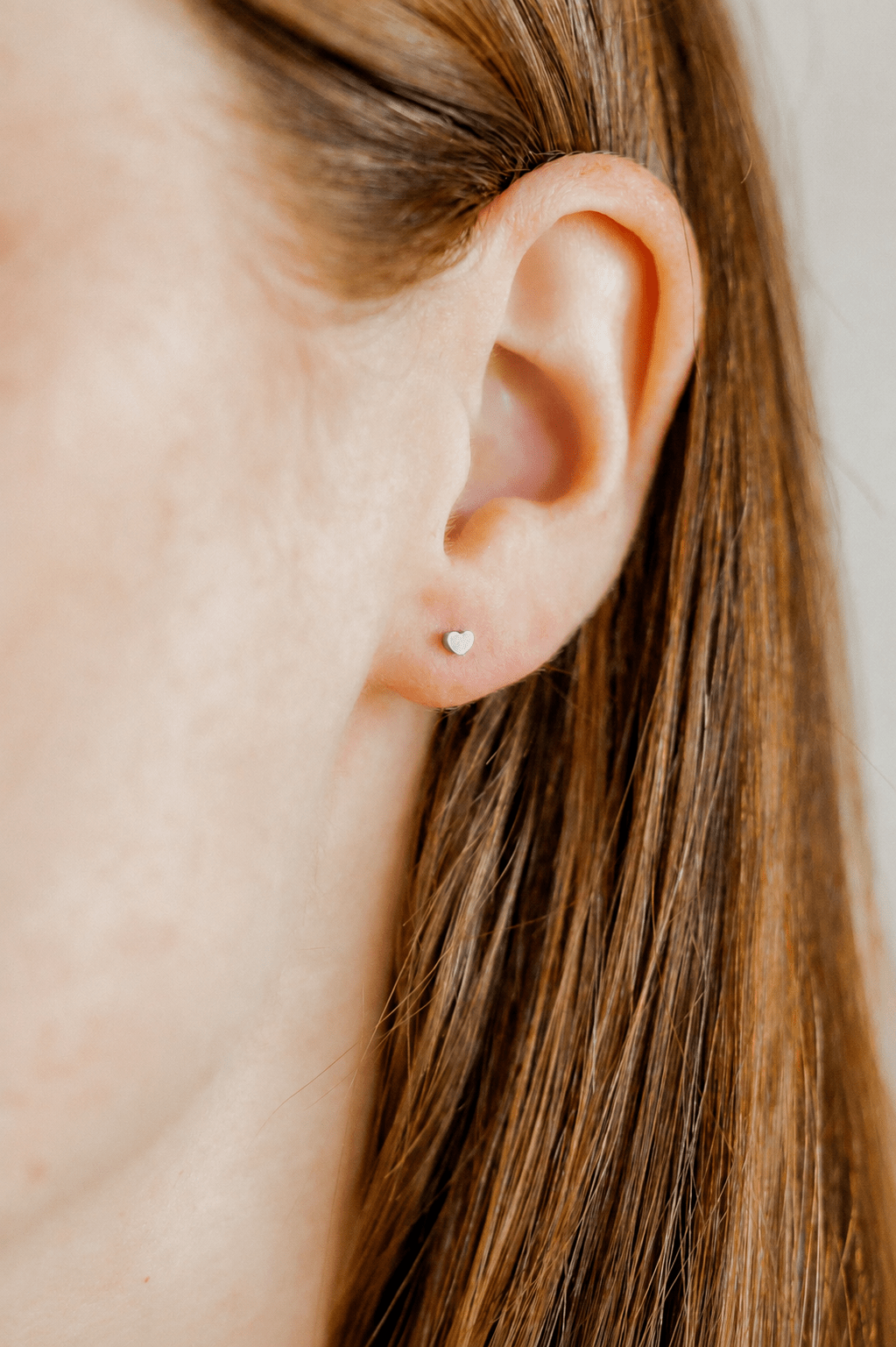 LINNY CO Micro Tessa Heart Silver screwback stud earrings for kids & little girls — hypoallergenic, waterproof stainless steel with secure screwback backs, shown on model.