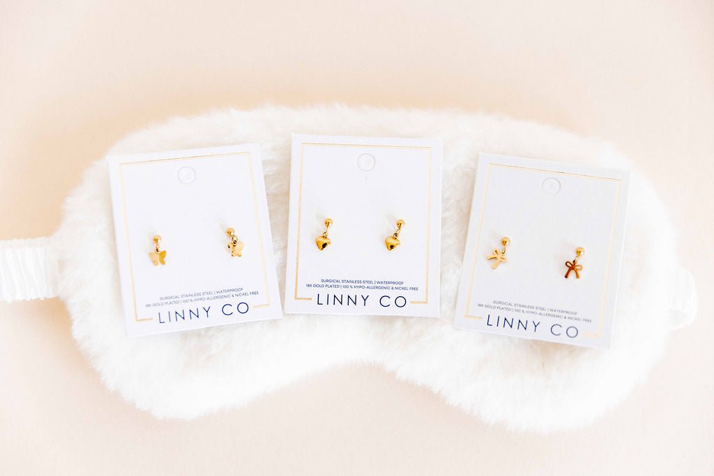LINNY CO Millie Bow screwback stud earrings for kids & little girls — hypoallergenic, waterproof stainless steel with secure screwback backs, flat-lay styling.