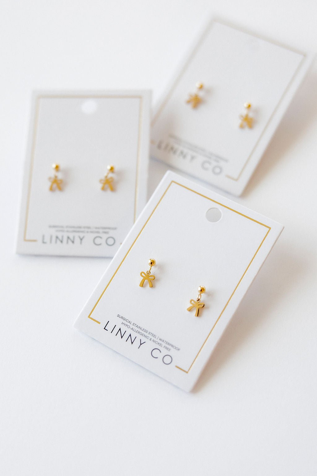 LINNY CO Millie Bow screwback stud earrings for kids & little girls — hypoallergenic, waterproof stainless steel with secure screwback backs, flat-lay styling.