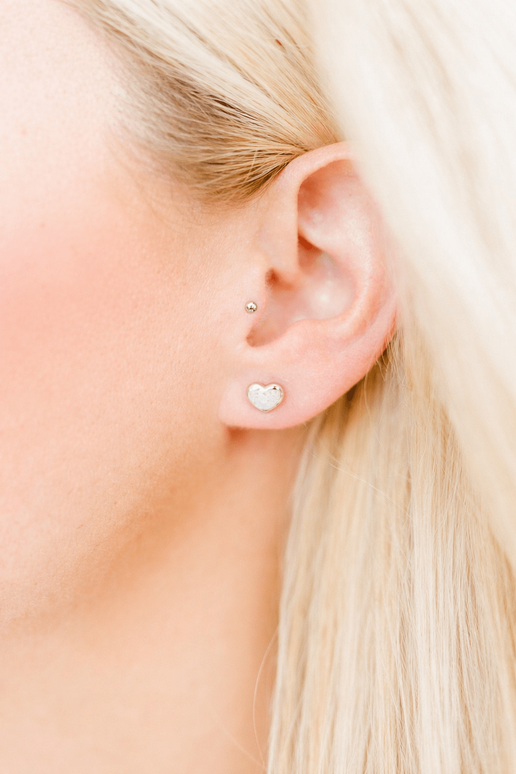 LINNY CO Nora Heart White Silver screwback stud earrings for kids & little girls — hypoallergenic, waterproof stainless steel with secure screwback backs, shown on model.