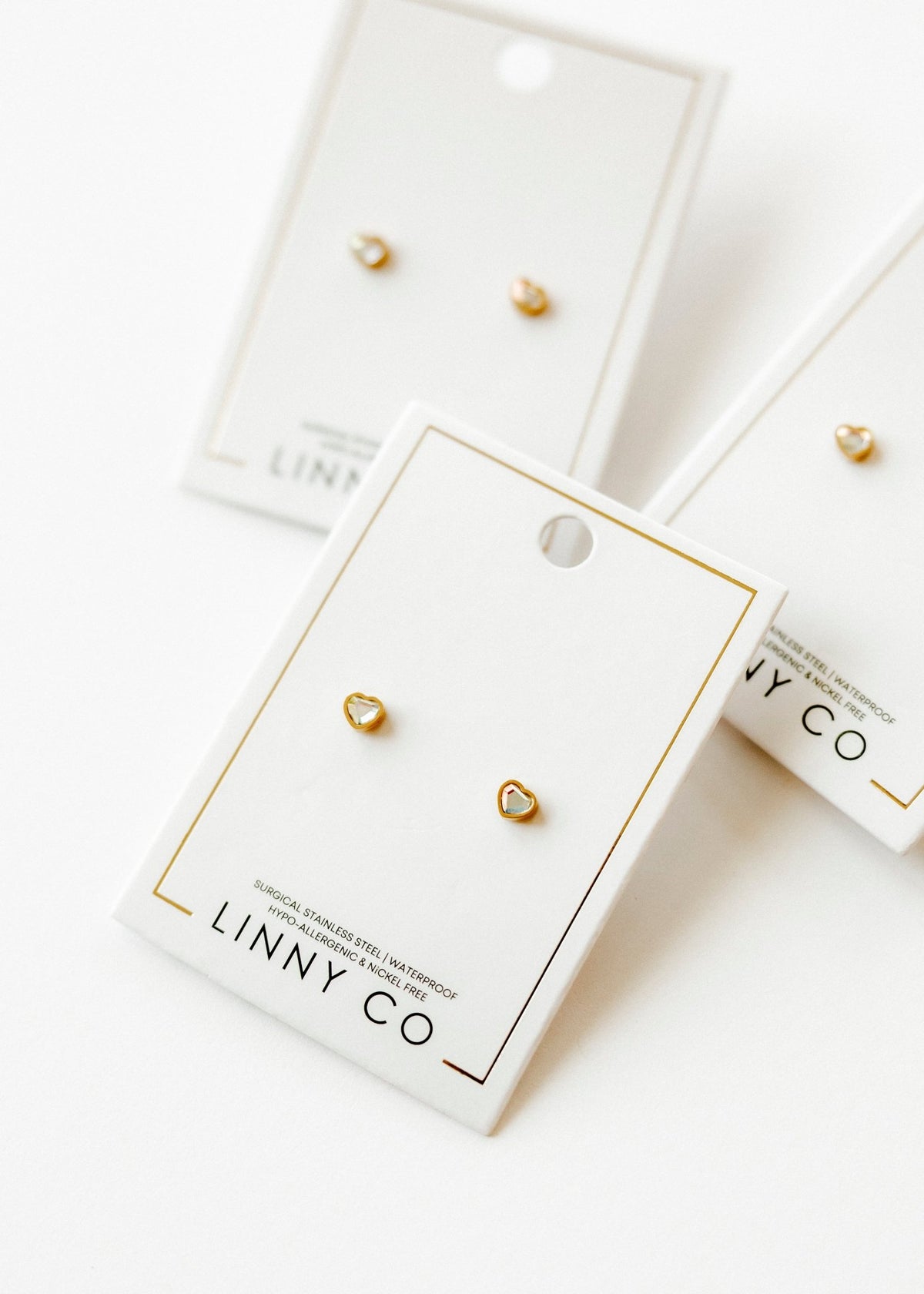LINNY CO Polly Heart screwback stud earrings for kids & little girls — hypoallergenic, waterproof stainless steel with secure screwback backs, flat-lay styling.