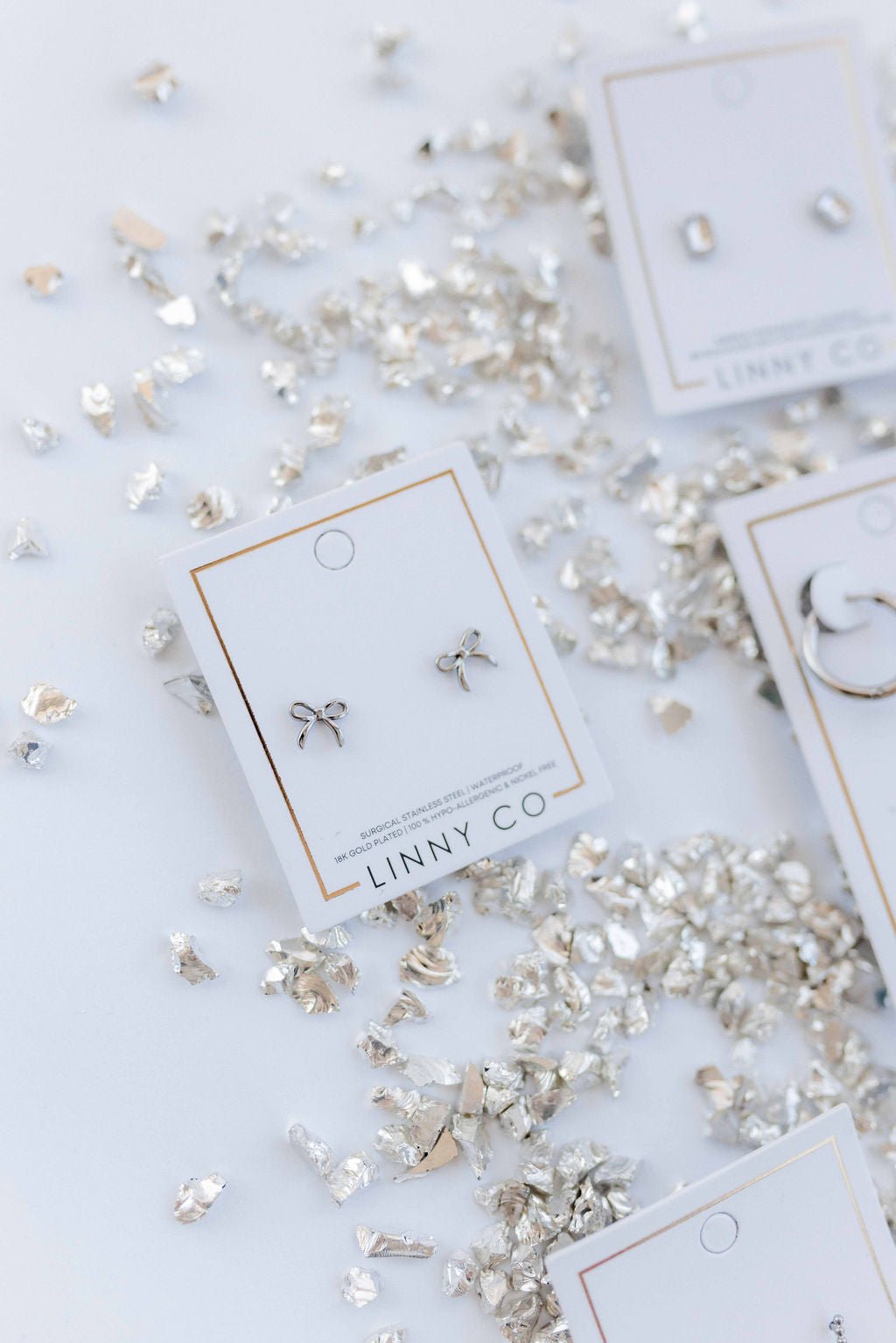 LINNY CO Sadie Bow Silver screwback stud earrings for kids & little girls — hypoallergenic, waterproof stainless steel with secure screwback backs, flat-lay styling.