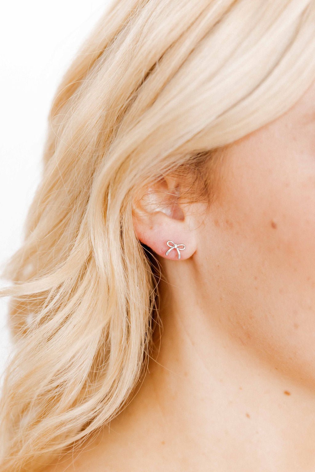 LINNY CO Sadie Bow Silver screwback stud earrings for kids & little girls — hypoallergenic, waterproof stainless steel with secure screwback backs, shown on model.